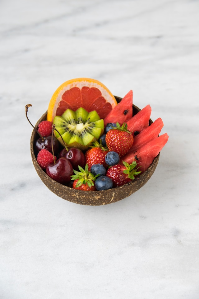 A brown bowl filled with fruit including grapefruit, kiwi, watermelon, strawberries, raspberries, blueberries and cherries.